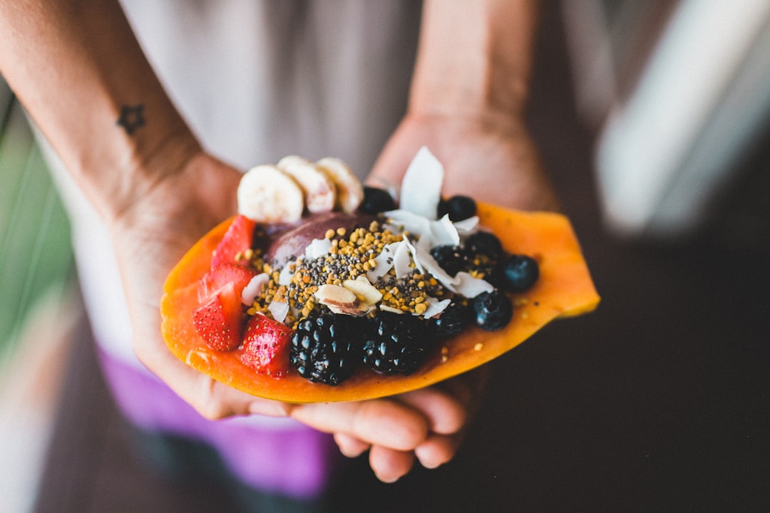 person holding blue berry with strawberry dessert shallow focus photography / Photo by Epicurrence o