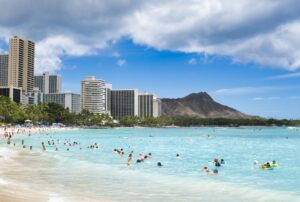 People swim in the ocean near a tropical beach with buildings.