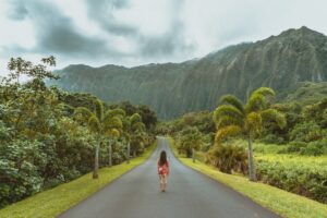 a woman walking down a road in the middle of a forest
