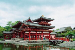 Historic japanese temple with red pillars reflected in water.
