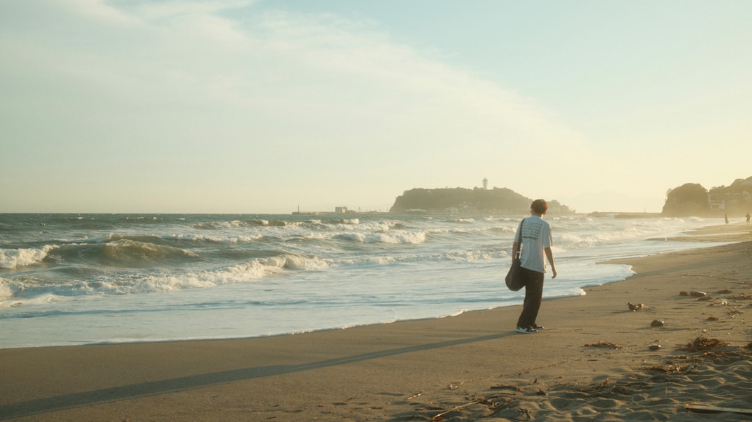 Person walks on sandy beach with ocean waves at sunset