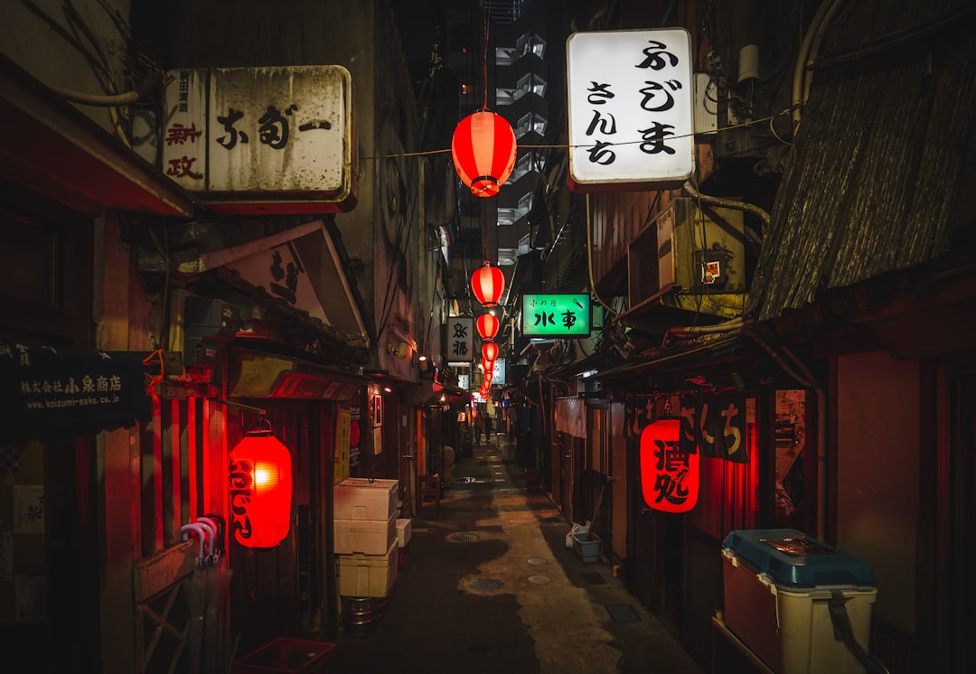 A narrow alleyway in Tokyo at night with glowing red lanterns and illuminated signs